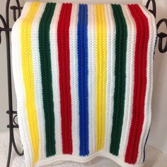 a crocheted blanket with multicolored stripes on the front and back, hanging from a wrought iron rack