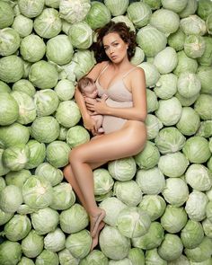 a woman in a bathing suit is holding a baby while surrounded by large cabbages