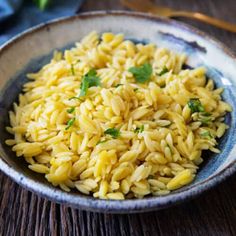 a bowl filled with yellow rice on top of a wooden table