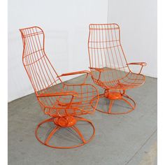 two orange chairs sitting next to each other on top of a cement floor in front of a white wall