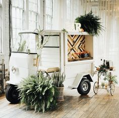 a small white truck parked in front of a window filled with potted plants and greenery