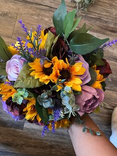 a bridal bouquet with sunflowers, roses and greenery is being held by someone's hand