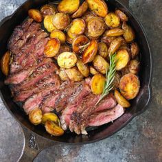 steak and potatoes in a cast iron skillet on a stone counter top with a sprig of rosemary