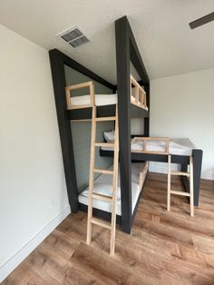 two bunk beds in a room with wood floors and white walls, one has a ladder that leads to the second bed