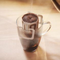 a hot chocolate drink in a glass cup with steam coming out from the top, on a wooden table