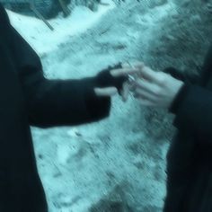 two people standing outside in the snow holding something up to their hands with one hand