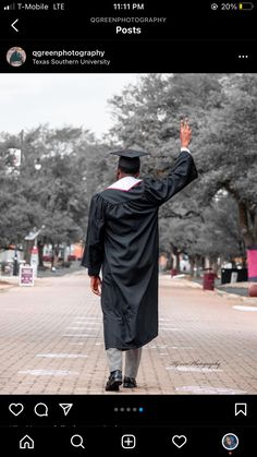 a man in a graduation gown is walking down the street with his hand raised up