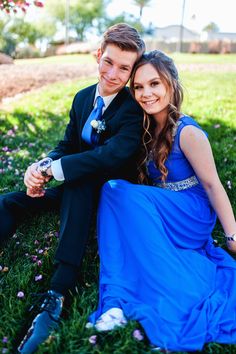 a young man and woman in formal wear sitting on the grass smiling at the camera