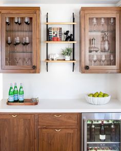 a kitchen with wooden cabinets and white counter tops, filled with wine glasses and bottles