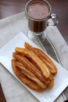 a white plate topped with churros next to a cup of hot chocolate on top of a table