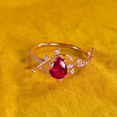 a gold ring with a red stone surrounded by white diamonds on a yellow cloth background