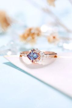 an engagement ring with blue and white diamonds on top of a piece of paper next to flowers