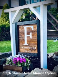 a wooden sign with the letter f on it and flowers growing in front of it