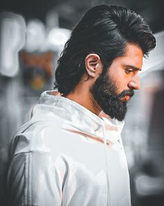 a man with black hair and beard wearing a white jacket looking off to the side