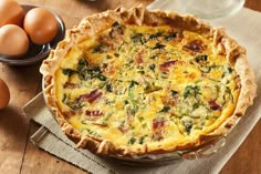 a quiche with bacon, spinach and eggs on a wooden table next to an egg bowl