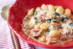 a red bowl filled with pasta and spinach on top of a checkered table cloth