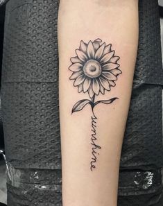 a sunflower tattoo on the arm with words written in cursive writing below it