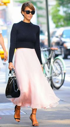 a woman walking down the street in a pink skirt and black sweater with her handbag