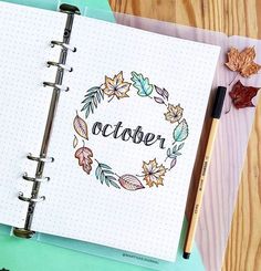 an open notebook with the word october written in it next to a pen and autumn leaves