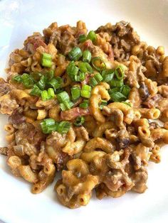 a white plate topped with macaroni and cheese covered in ground beef, green onions and seasonings