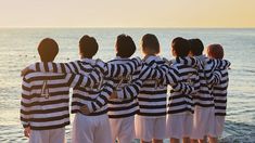 five people in jail uniforms standing on the beach looking out at the ocean and water