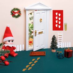 an elf is sitting in front of a door with christmas decorations on the table next to it