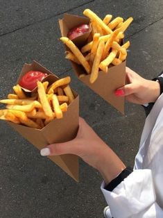 two people holding up some fries with ketchup and tomatoes in them on the street