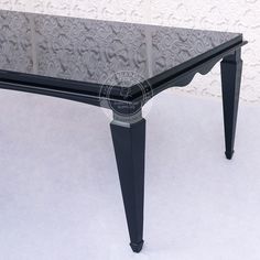 a black glass table with metal legs in front of a wall