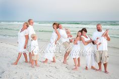 a group of people standing on top of a sandy beach next to the ocean in white outfits