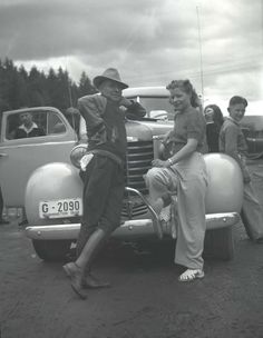 an old black and white photo of people standing next to a car