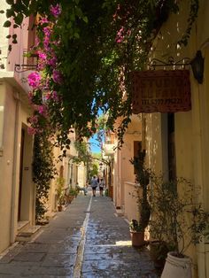 an alley way with people walking down it and pink flowers on the trees overhangs