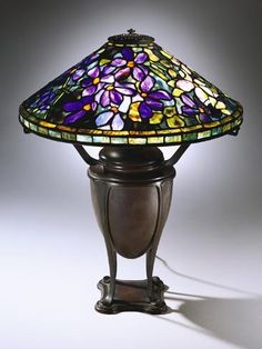 a stained glass table lamp sitting on top of a wooden stand with a metal base