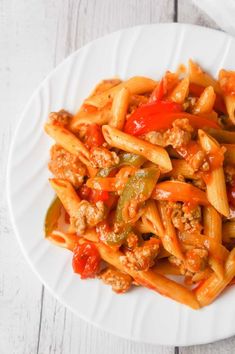 a white plate topped with pasta and meat covered in sauce on top of a wooden table