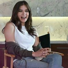 a woman sitting in a chair smiling and holding a book with her right arm wrapped around her leg