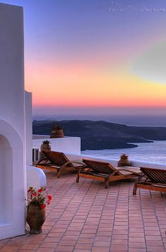 the sun is setting over the ocean and lounge chairs are set up on the patio