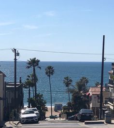 cars parked on the side of an empty street next to the ocean and palm trees