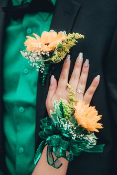 a person in a suit and tie with flowers on their wrist, holding onto another man's hand