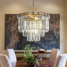 a chandelier hanging over a dining room table with white chairs and a potted plant