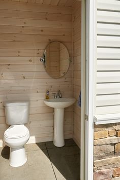 a white toilet sitting next to a sink in a bathroom under a mirror on top of a wooden wall