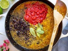 a pan filled with black beans and sauce next to sliced limes on the side