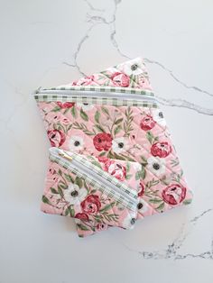 two pink floral pouch bags sitting on top of a marble counter