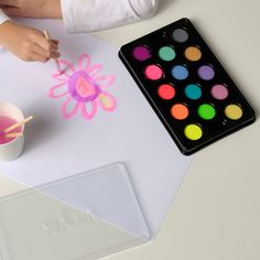 a child is painting with watercolors on a paper next to a plastic cup