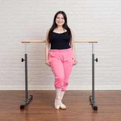 a woman standing in front of a wooden table with a black top and pink pants