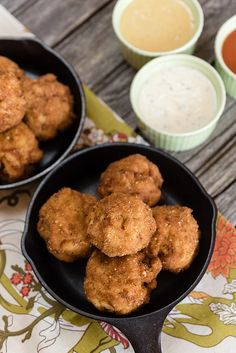 two black pans filled with fried food on top of a table next to dipping sauce