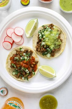 two tacos on a white plate with pickles and sauces next to them