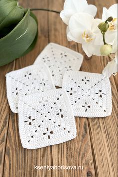 three crocheted coasters sitting on top of a wooden table next to flowers