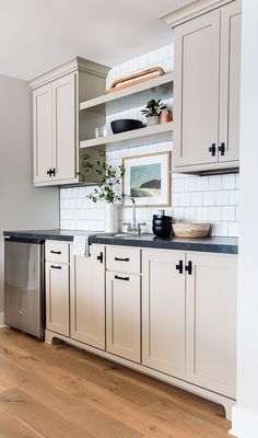 a kitchen with white cabinets and black counter tops is pictured in this image, there is a dishwasher on the left side of the cabinet