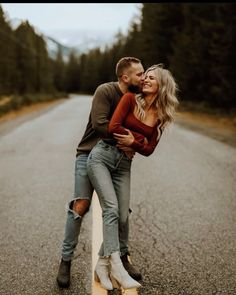 a man and woman hugging on the side of an empty road with trees in the background