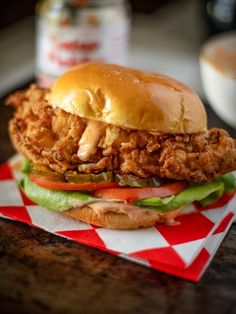 a chicken sandwich with lettuce, tomato and pickles on a checkered napkin