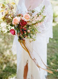 a woman in a white dress holding a flower bouquet on her wedding day with grass and trees behind her